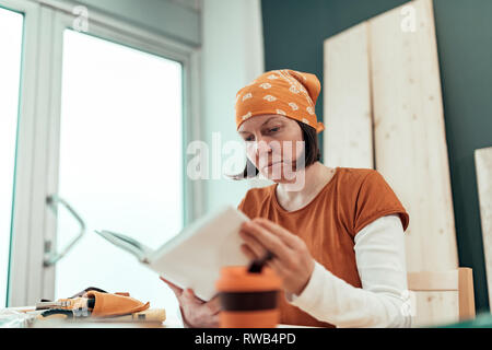 Female carpenter reading DIY project instruction manual in small business woodwork workshop Stock Photo