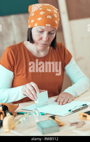 Self employed female carpenter is stamping project documentation in small business woodwork workshop Stock Photo