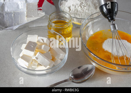 Diced butter in a bowl on the table. Eggs in a glass bowl with sugar. Stock Photo