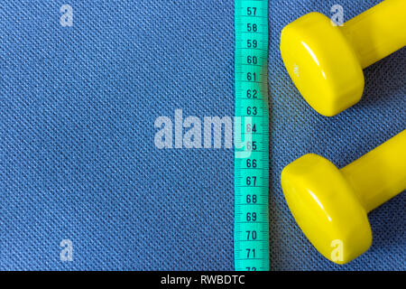 Yellow dumbbells and green measuring tape on blue fitness mat Stock Photo