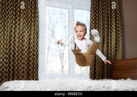 child fun home. Cheerful boy in motion jumping laughing on bed. Little kid of 6 years old happily plays morning in room.