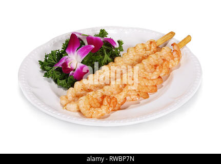 Shrimp skewers according to Chinese tradition. Served on a white plate with salad decoration. Stock Photo