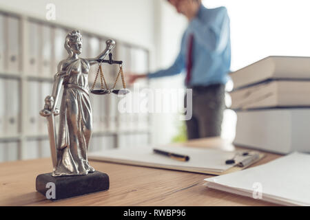 Attorney talking on mobile device in law office, selective focus on statue of Lady Justice Stock Photo