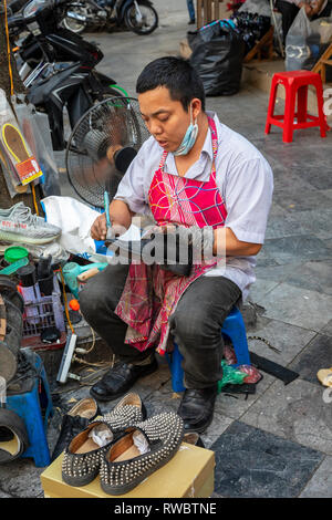 Man working as a cobbler , repairing shoes, on the pavement in the Old Quarter of Hanoi, Vietnam, Asia Stock Photo