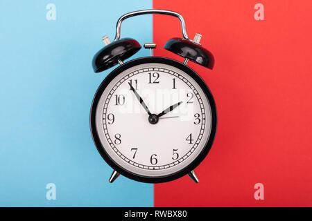 black metal arrow alarm clock on blue-red background Stock Photo