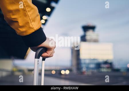 Hand of the young man holding luggage against airport terminal. Stock Photo