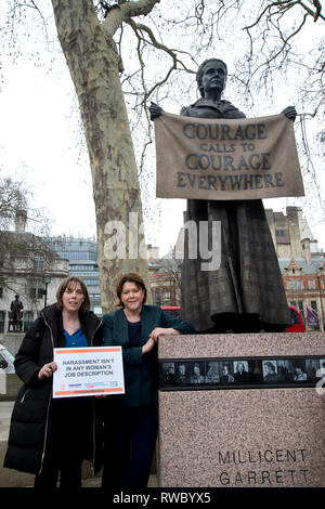Parliament Square, Westminster, London. Celebration for International Women's Day. Maria Miller, Conservative MP for Basingstoke with Jess Phillips, the Labour MP for Birmingham Yardley in front of the statue of suffragette Millicent Garrett Fawcett with a sign saying 'Harassment isnt in any woman's job description'. Credit: Jenny Matthews/Alamy Live News Stock Photo