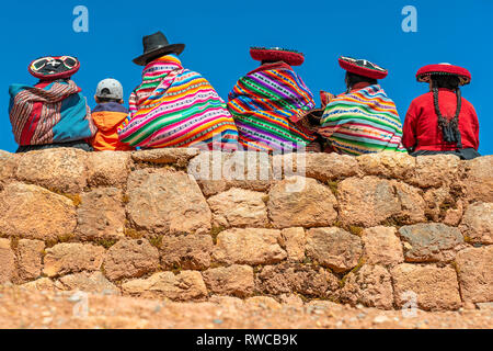 Indigenous Peruvian Quechua women in traditional clothing with a boy sitting on an ancient Inca wall in the ruin of Chinchero, Cusco province, Peru. Stock Photo