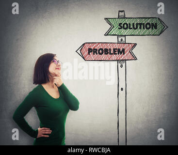 Positive thinking girl holding hand under chin looking up as drawn arrows of a signpost showing solution and problem directions to right and left side Stock Photo