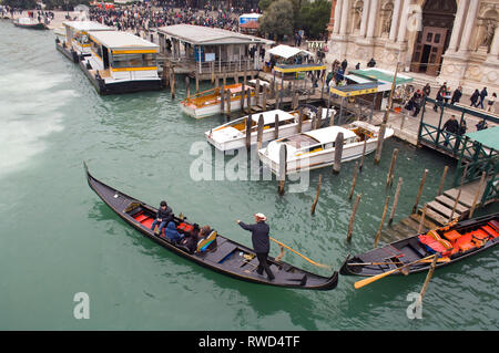A Gondolier steering a Gondola among other boats including the river bus stop in Venice, Italy, near the train station. Stock Photo