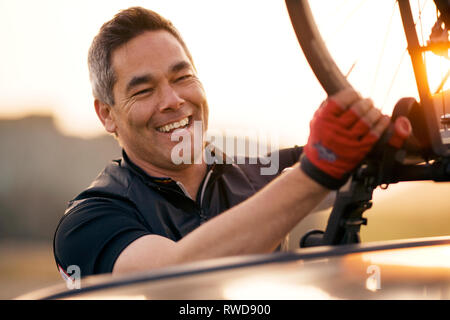 Mature man lifting his bike off a car Stock Photo