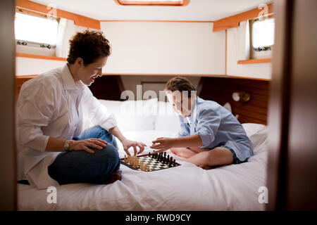 Mother and son playing chess in the bedroom of a boat Stock Photo