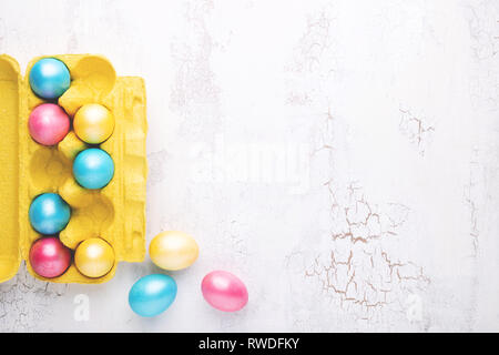 Colorful Easter eggs in egg tray on white craquelure table. Holiday background with copy space, top view. Stock Photo