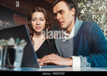 Young man and woman working in front of the laptop. Team meeting,work process. Project managers near window. Analyze business plans. Stock Photo