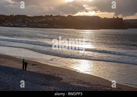 Ballycastle, Northern Ireland, UK. Atlantic coast. Beach, waves and unrecognizable pair in sunset light reflection with dark heavy clouds Stock Photo