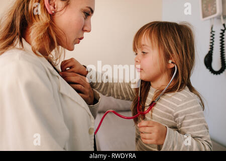 Cute girl pretending to a doctor examining the heart rate of her pediatrician at hospital. Girl patient playing with her doctor in clinic. Stock Photo