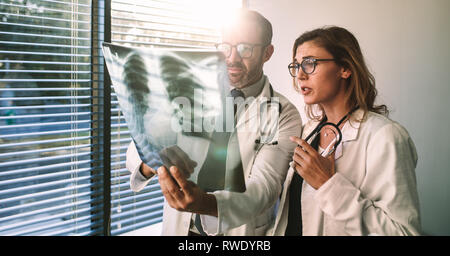 Doctors colleagues look at the x-ray of the patient and discussing over the treatment. Male and female doctors looking at x-ray film and diagnosing pa Stock Photo