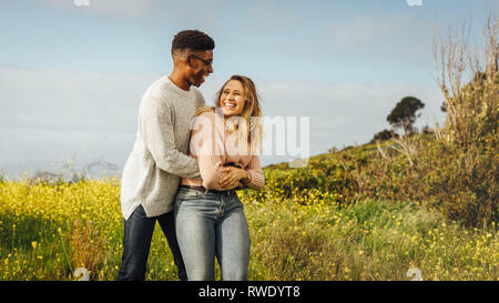 Happy couple having fun together outdoors in meadow. African man and caucasian woman enjoying a quality time together. Stock Photo