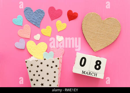 wooden March 8 calendar next to paper colorful hearts over pink wooden background Stock Photo