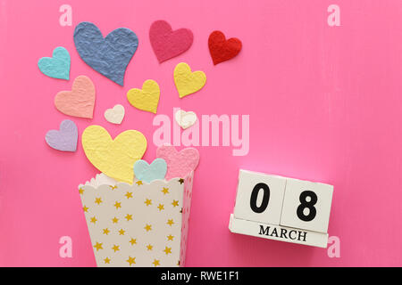 wooden March 8 calendar next to paper colorful hearts over pink wooden background Stock Photo