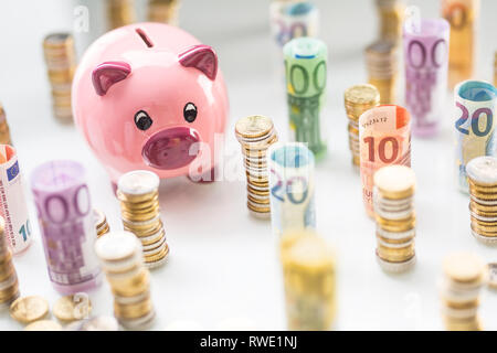 Pink piggy bank in the middle of rolled euro banknotes and towers with coins Stock Photo