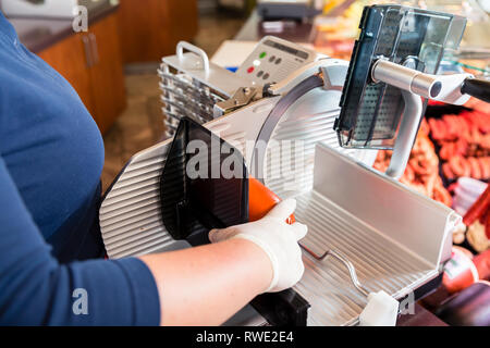 Woman in butcher shop cutting bacon with machine Stock Photo