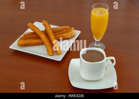 Traditional spanish churros with hot chocolate sauce  and orange juice, on a wooden table Stock Photo