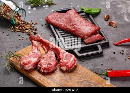 Set of Raw uncooked black angus beef tomahawk steaks on bones and veal tenderloin served with chilli and peppercorns. Rustic style. Close up Stock Photo