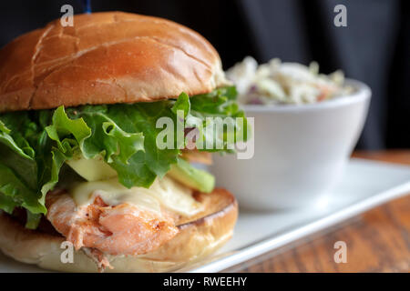 Grilled salmon on a toasted bun with lettuce and cheese, served with a small bowl of coleslaw Stock Photo