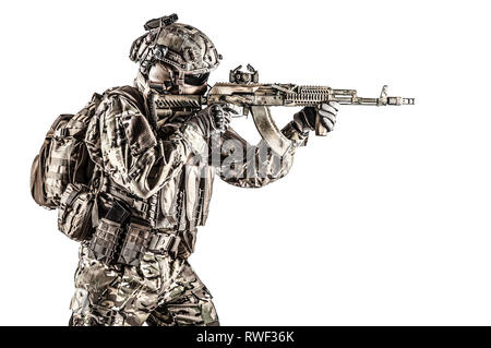 Operador das forças de operações especiais russas com rifle de assalto  kalashnikov, mochila militar e capacete de combate, disparando uma arma no  deserto da síria. ruínas antigas e helicópteros
