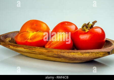 Fresh and juicy persimmon fruits on wooden plate. Stock Photo