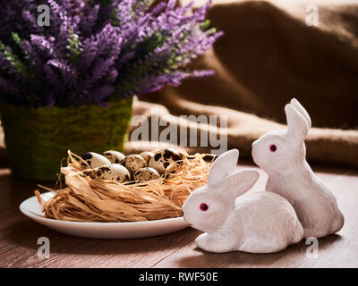 Easter composition rabbits with eggsa on wooden background, Easter background with Easter eggs in nest and spring flowers. Top view with copy space. Stock Photo