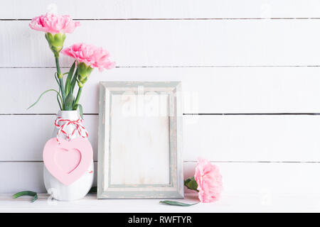 Valentines day and love concept. Pink carnation flower in vase with old vintage picture frame and red heart and on white background. Stock Photo