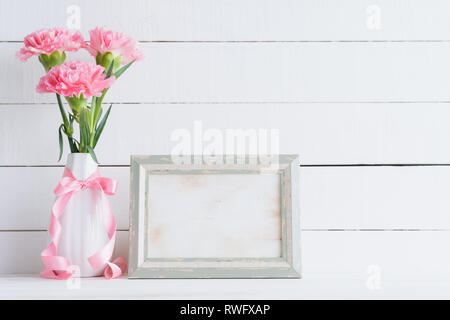 Valentines day and love concept. Pink carnation flower in vase with old vintage picture frame and red heart and on white background. Stock Photo