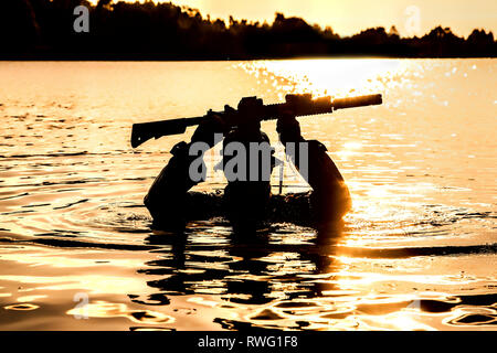 Silhouette of a special forces soldier holding weapon above head while crossing a river. Stock Photo