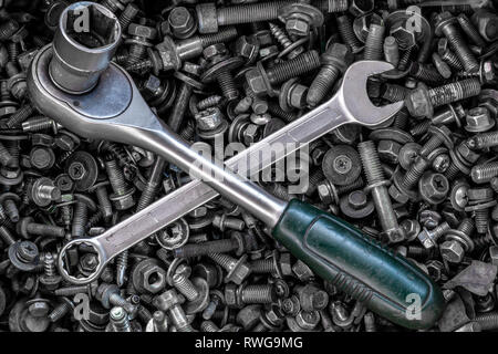 Flat Lay metal wrenches and ratchet of different sizes lie on the background of various metal cogs, screws and nails, top view. Close-up Carpenter's T Stock Photo