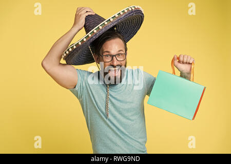 Mexican shopping. Man smiling face in sombrero hat shopping yellow background. Guy with beard looks festive in sombrero. Holiday sales concept. Man in festive mood shopping traditional sales season. Stock Photo