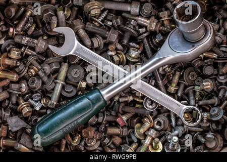 Flat Lay metal wrenches and ratchet of different sizes lie on the background of various metal cogs, screws and nails, top view. Close-up Carpenter's T Stock Photo