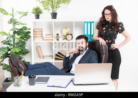 Typical office life. Man bearded hipster boss sit in leather armchair office interior. Boss and secretary girl at workplace. Relations at work. Business people and staff concept. Lazy boss office. Stock Photo