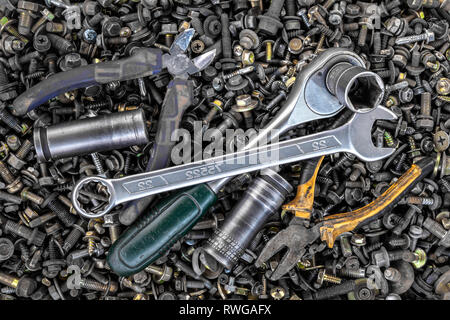 Flat Lay metal wrenches, ratchet, pliers, interchangeable tool heads of different sizes lie on the background of various metal cogs, screws and nails, Stock Photo
