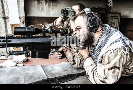 Navy SEAL sniper team engaging targets from a ruined building with a sniper rifle. Stock Photo