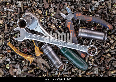 Flat Lay metal wrenches, ratchet, pliers, interchangeable tool heads of different sizes lie on the background of various metal cogs, screws and nails, Stock Photo
