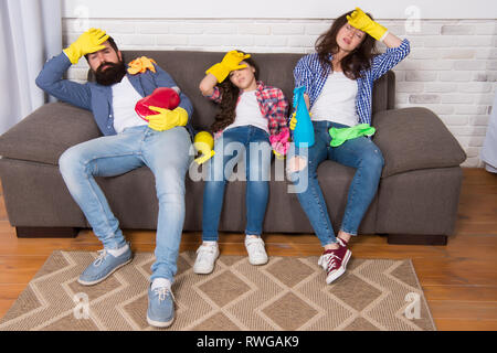 Cleaning all day exhausting occupation. Tired parents and kid. Exhausting cleaning day. Family mom dad and daughter with cleaning supplies sit on couch. Family care about cleanliness. Finish cleaning. Stock Photo