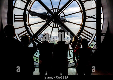 Tourists looking out from beyond the mechanism of huge clock on Musee D'Orsay facade Stock Photo