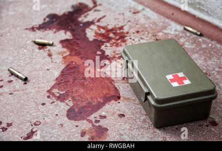 Military first aid kit on floor with empty bullet casings and fresh stains of human blood. Stock Photo
