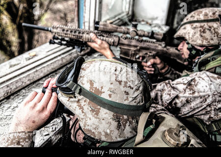 Sniper team shooting enemy targets with sniper rifle from inside a ruined urban building. Stock Photo