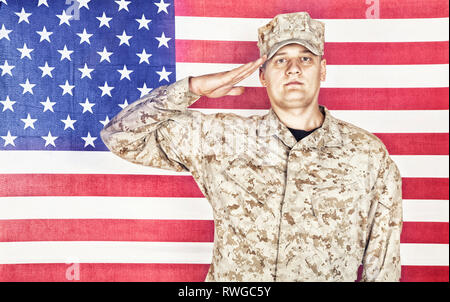 Portrait of U.S. soldier in camouflage uniform saluting American flag. Stock Photo