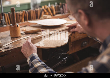 Over shoulder view of an instrument maker observing his workpiece with a wooden template Stock Photo