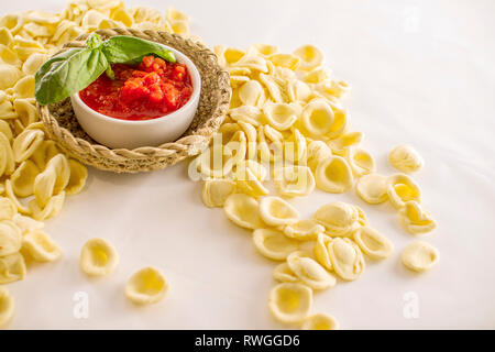 Close up still life of italian handmade pasta orecchiette pugliesi with tomato puree and basil on white background Stock Photo