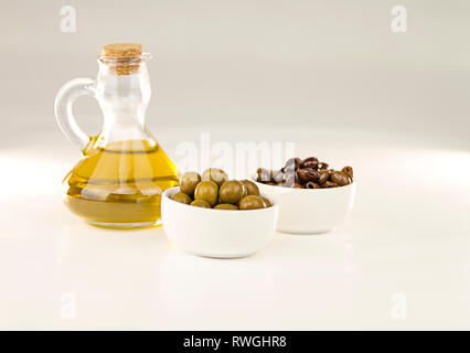 Close-up of a flask with extra virgin olive oil and two small cups with different varieties of olives on white background Stock Photo